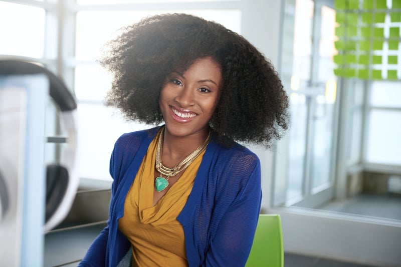 Portrait of a smiling woman with an afro at the computer in bright glass office.jpeg